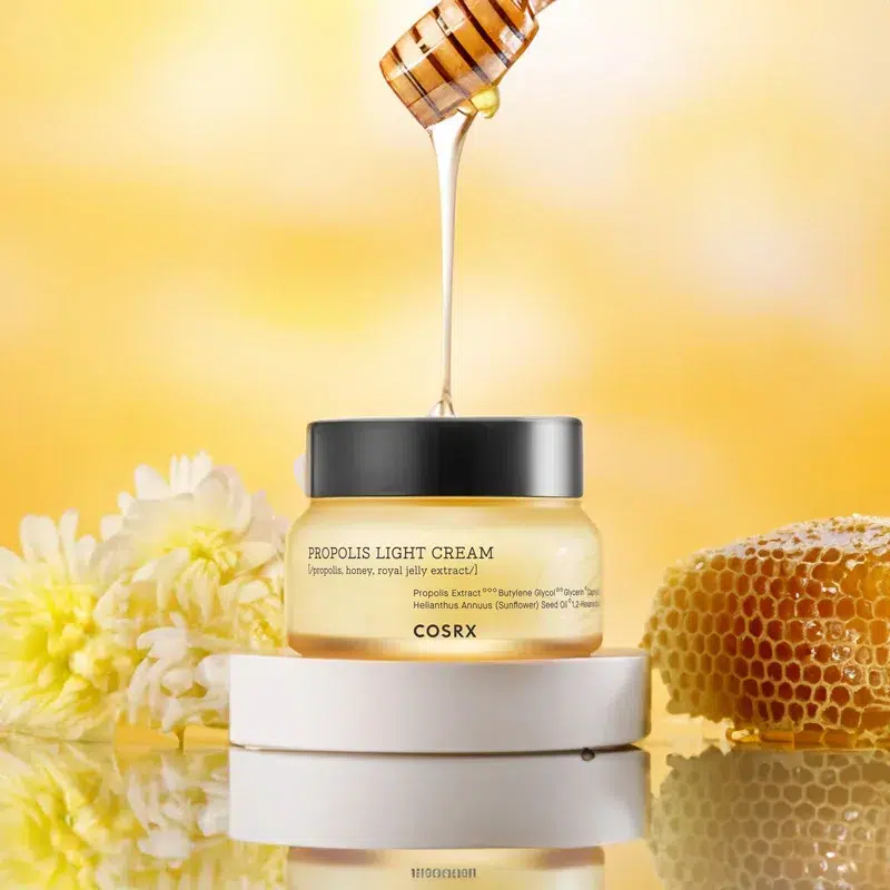 Cosrx Crème Hydratante Légère à la Propolis d'Abeille Noire Anti Imperfections 65 ml dans un pot avec du miel ruisselant d'une louche au-dessus