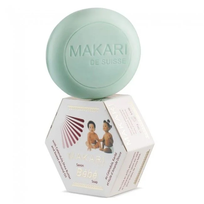 Un savon rond vert étiqueté « Makari de Suisse » repose sur une boîte hexagonale indiquant « Makari Bébé Savon au Calendula et Beurre de Karité 155 g »